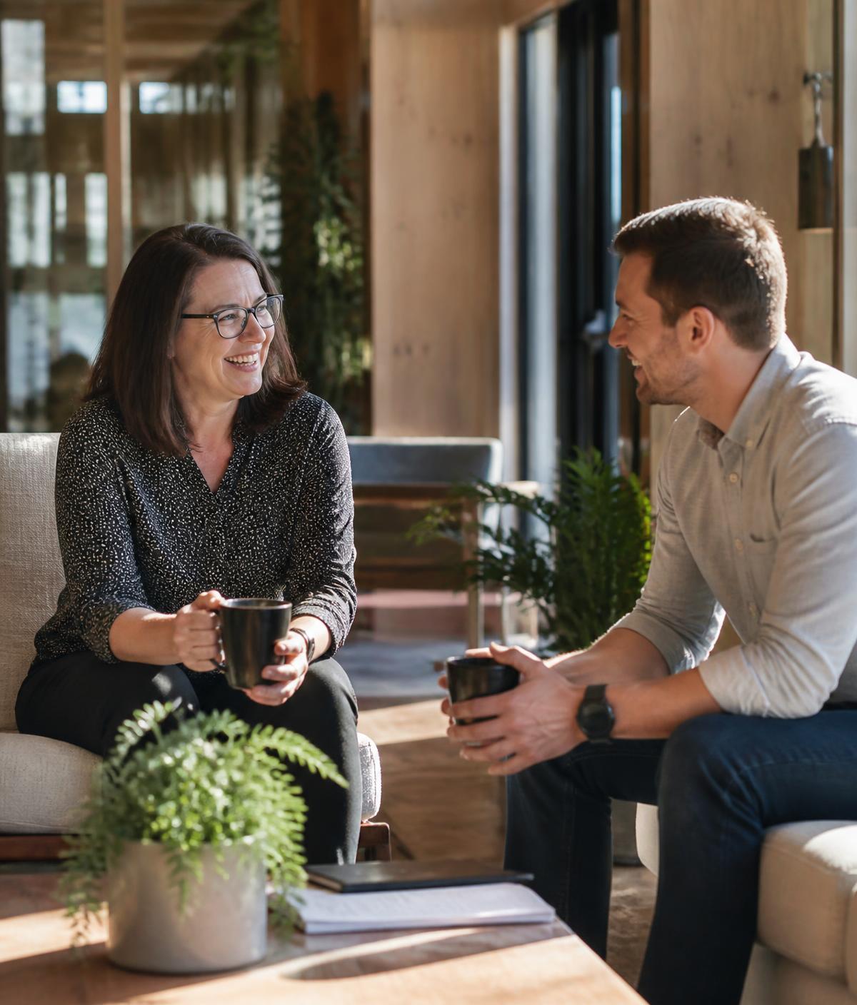 Two Australian care-sector professionals having a genuine conversation over coffee in a bright community workspace